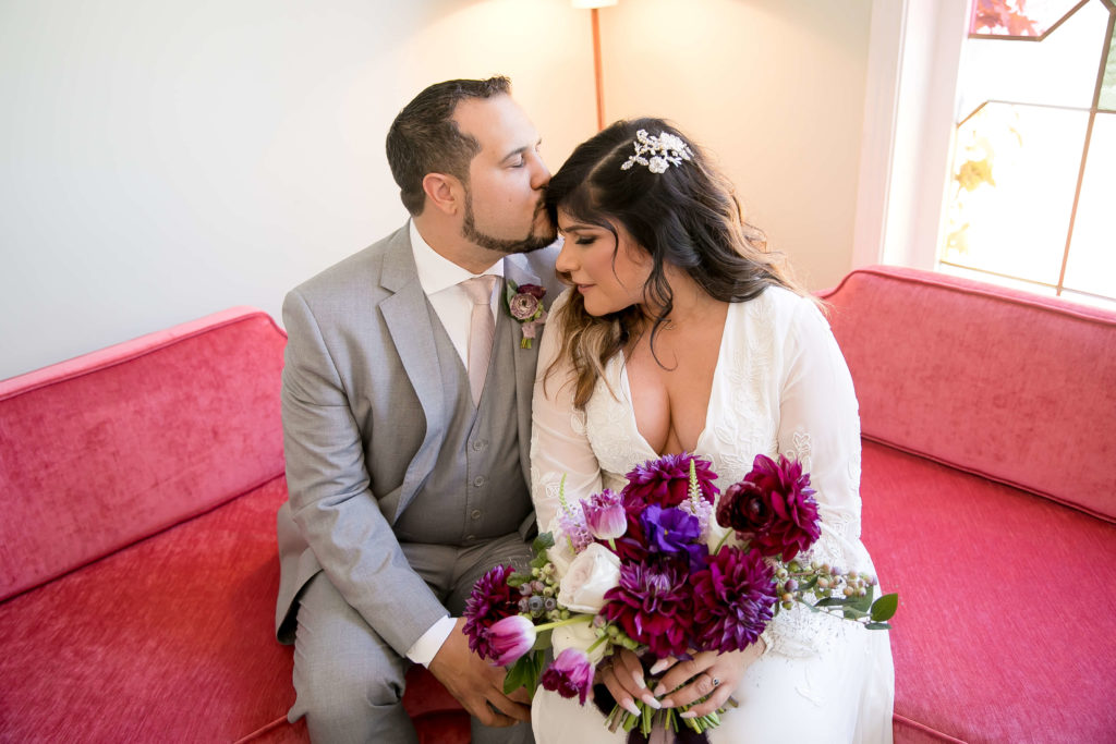 Groom and bride with a purple bouquet sitting on a pink couch at The Fig House Los Angeles
