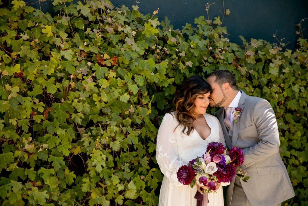 Bride holding a purple bouquet with groom in front of ivy wall at The Fig House Los angeles


