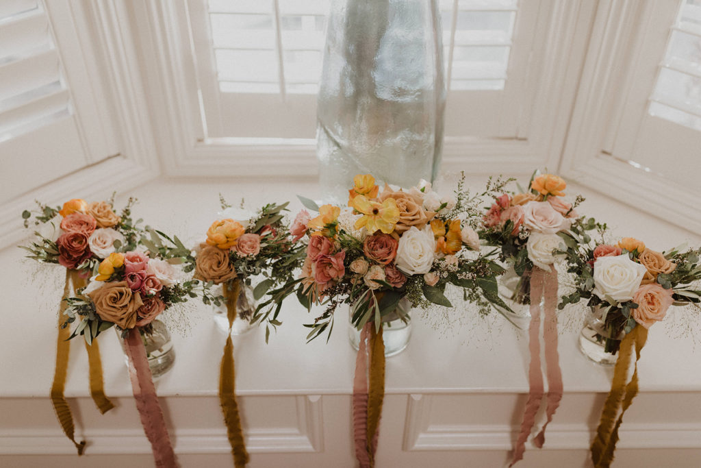 Fall wedding bouquets on a window sill with mauve orange and white flowers with gold and mauve ribbon from Tono + Co.