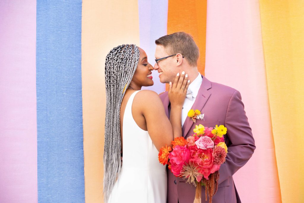 Bride and groom posing in front of colorful striped ceremony backdrop