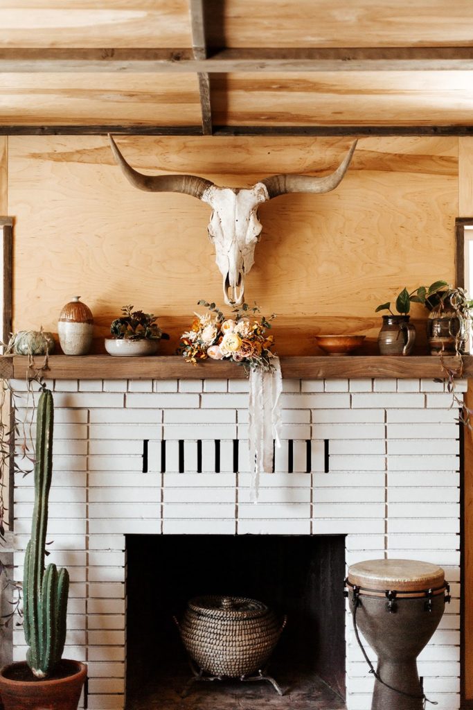 The Caravan house in Joshua Tree rustic fireplace with a mounted bull skull and a peach and white bridal bouquet 