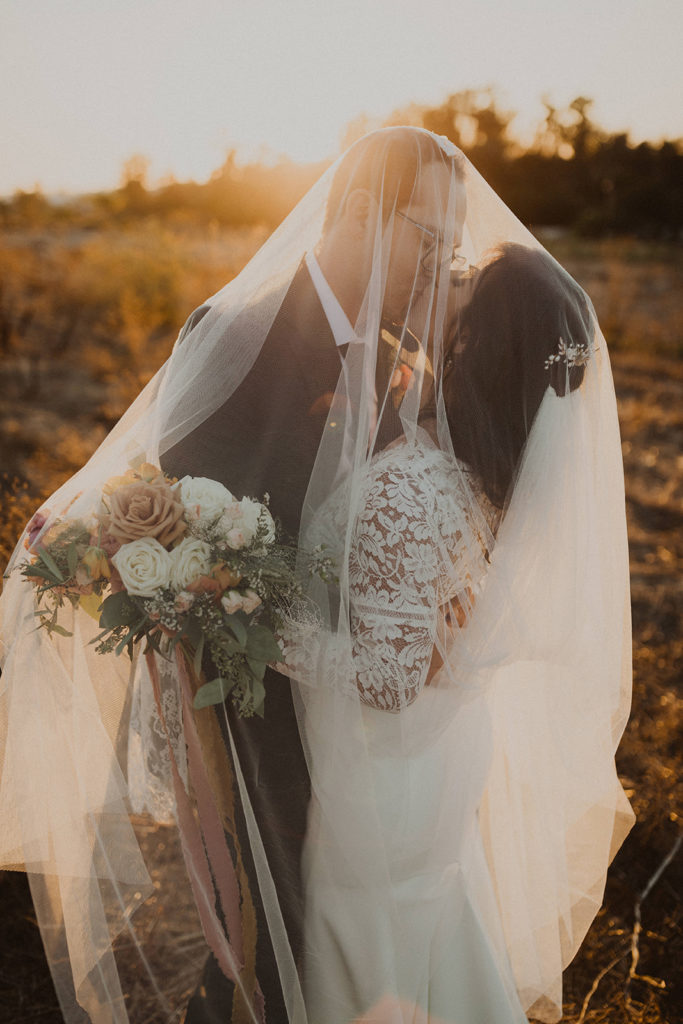 Outdoor Fall wedding couple kissing under the bridal veil with a colorful Fall bouquet in Vista California