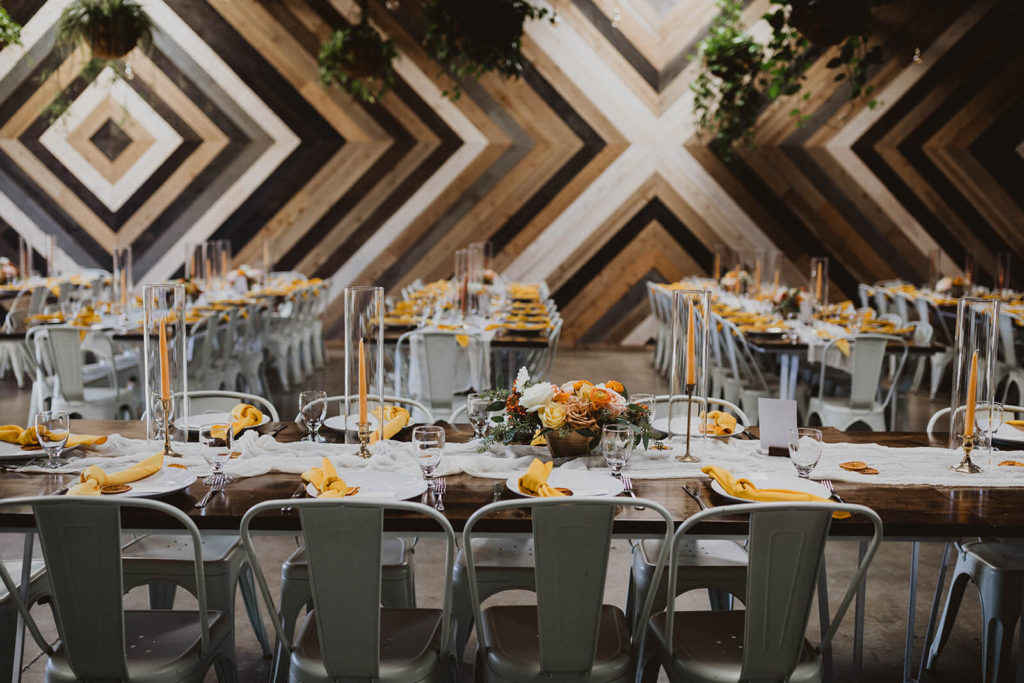 Modern Fall wedding reception with geometric wall backdrop and tables with yellow napkins and white metal chairs at The Wood Shed in Vista California