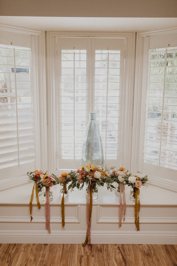 Fall wedding bouquets on a window sill with mauve orange and white flowers with gold and mauve ribbon from Tono + Co.