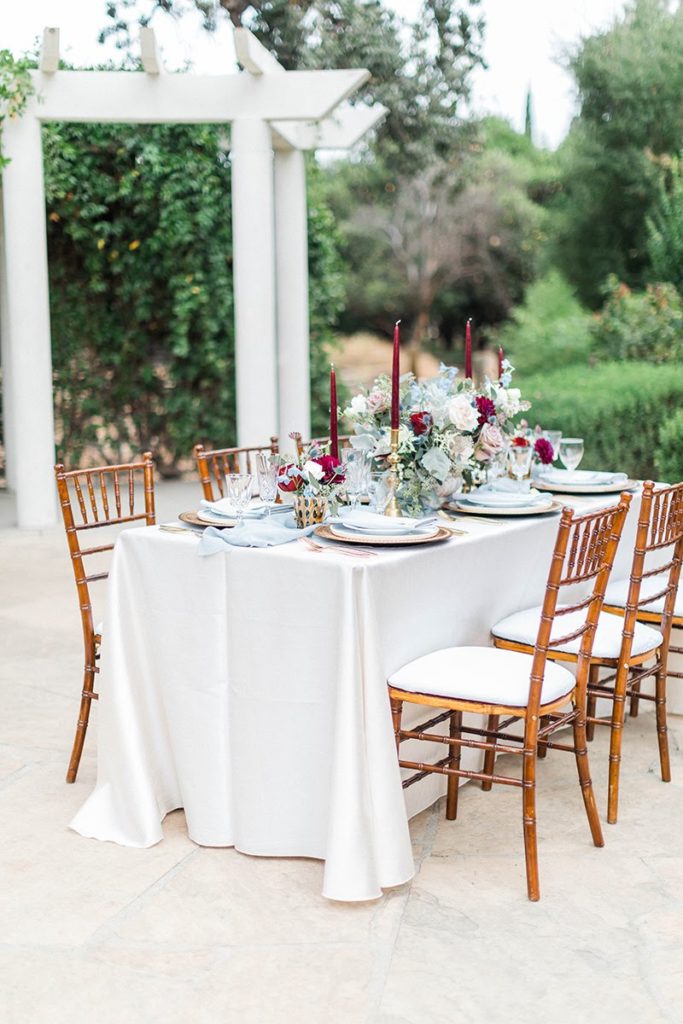 Organic blue and burgundy winter wedding reception table with gold silverware and burgundy taper candles at Orcutt Ranch