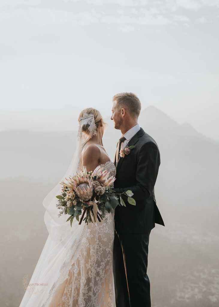 Bride in a white lace dress holding a large protea bouquet with her groom in a gray suit during their elopement ceremony in Yosemite