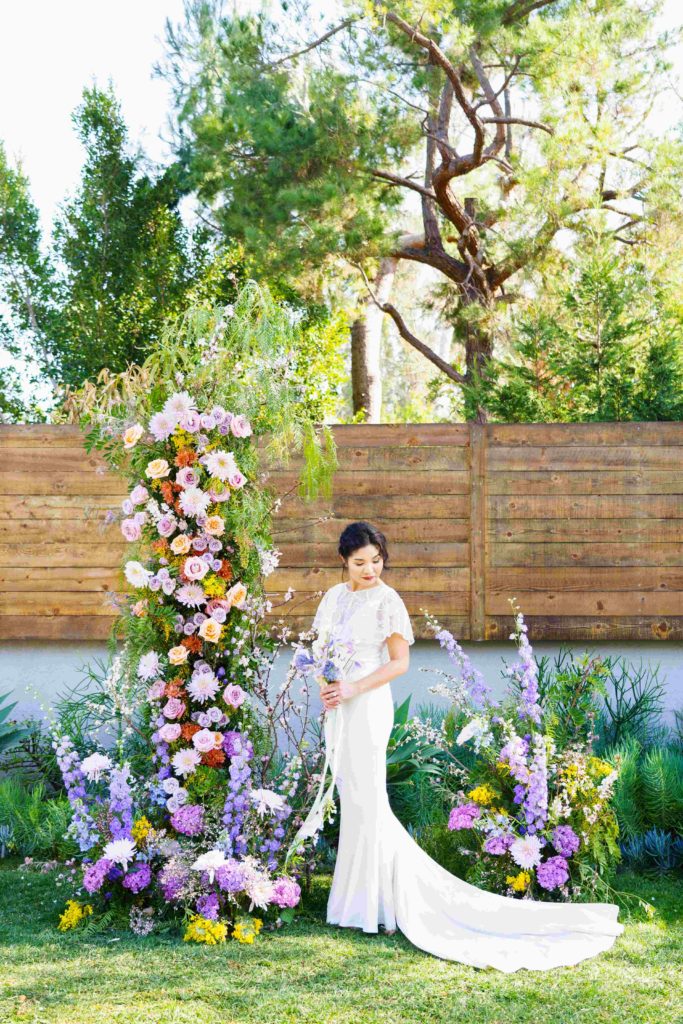 Beautiful Asian bride standing in a colorful garden inspired wedding arch