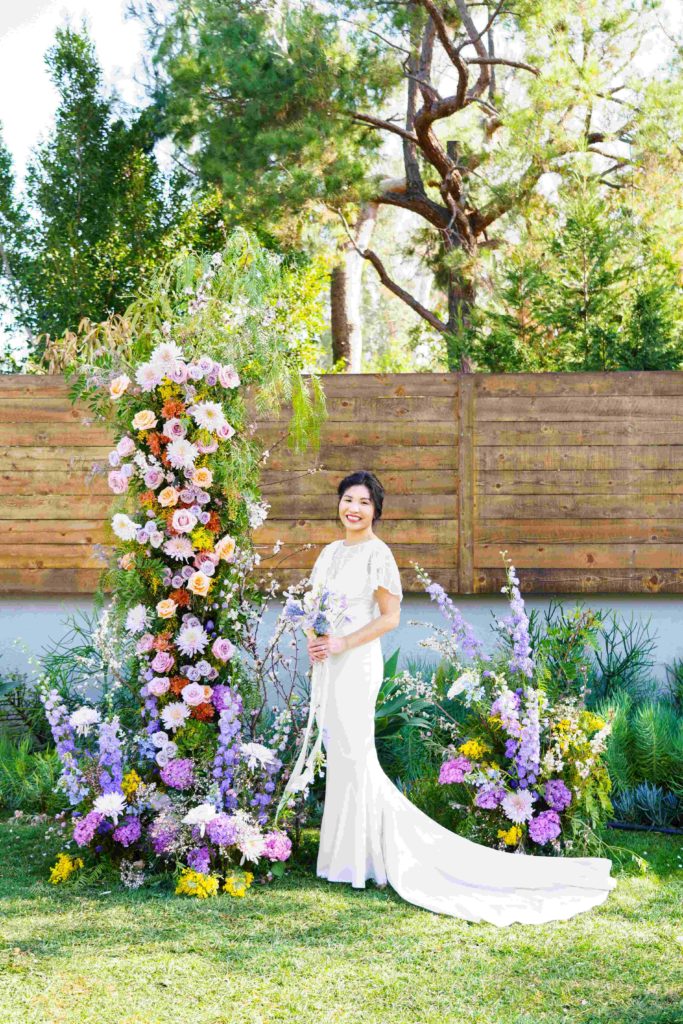 Beautiful Asian bride standing in a unique colorful wedding arch with colorful flowers