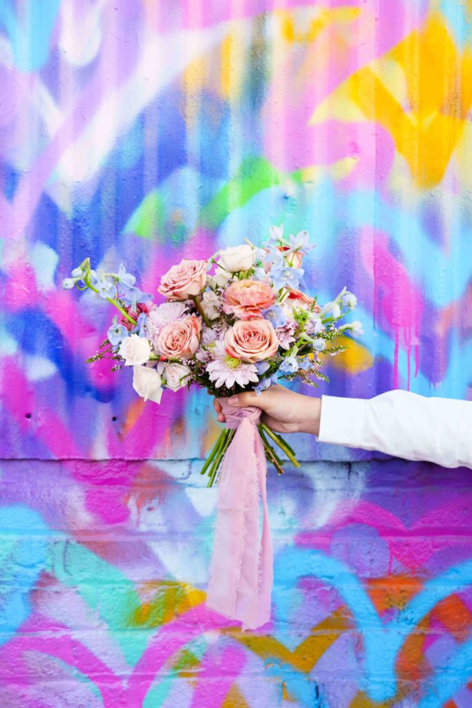 Colorful bouquet with a pink ribbon held in front of a graffiti wall