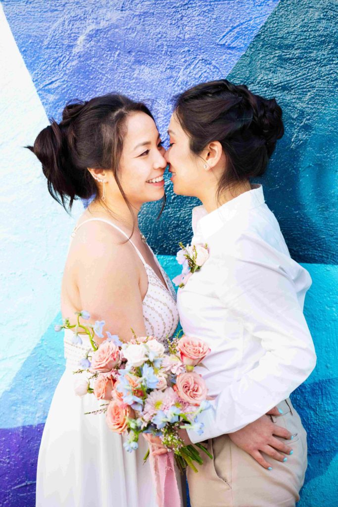 Lesbian couple embracing while holding a colorful wedding bouquet