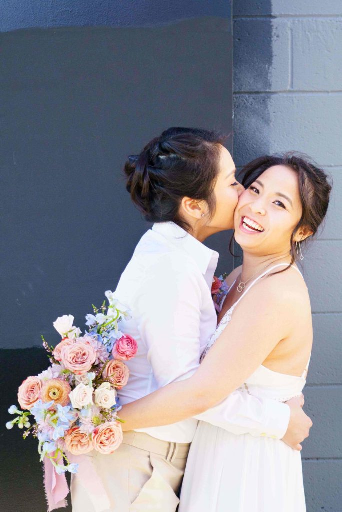 Lesbian couple kissing while holding a colorful bouquet 