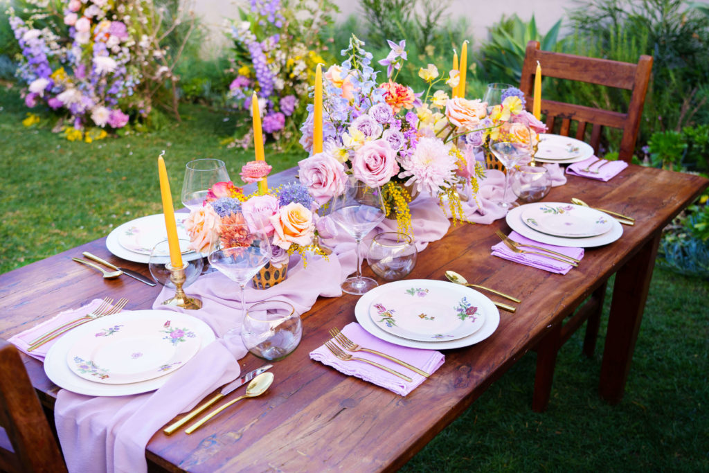 Small wooden table with colorful floral centerpieces and layered place settings for garden wedding