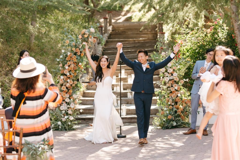 Bride and groom holding hands up after Rancho Las Lomas wedding ceremony