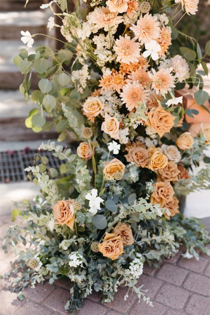 Peach and cream flowers with greenery on wedding floral arch