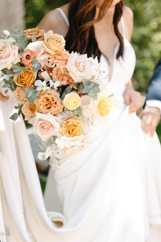 Bride carrying peach and cream bouquet with pops of yellow