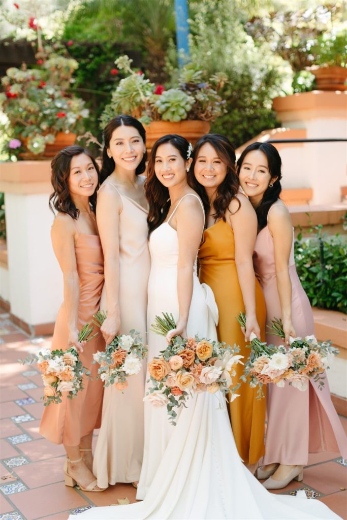 Bride and bridesmaids wearing silk gowns and holding floral bouquets