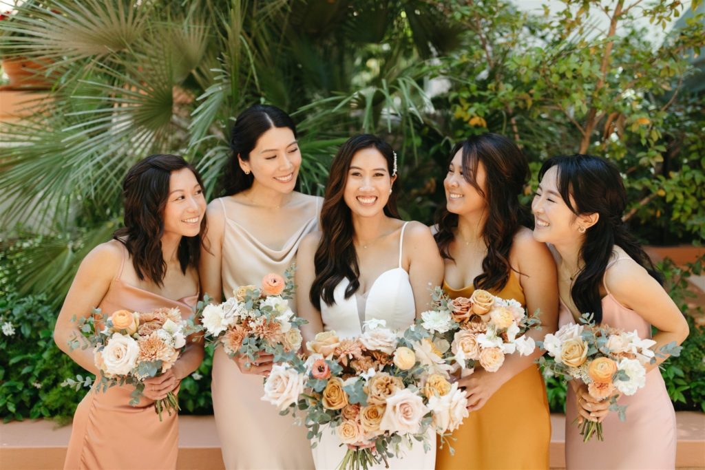Bride and bridesmaids smiling holding peach and cream bouquets