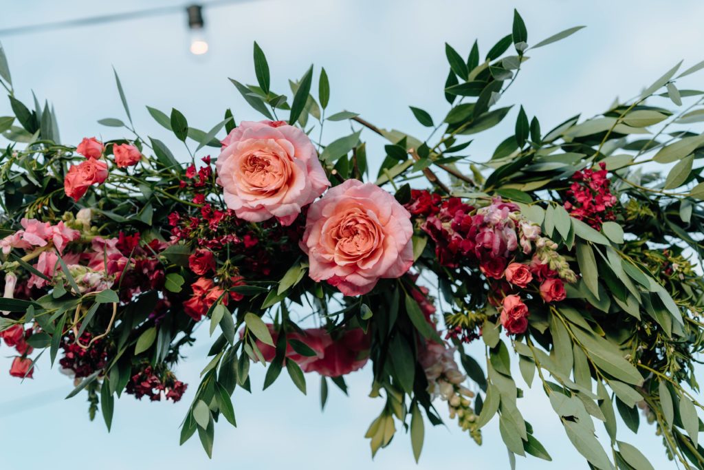 Greenery and pink and red flowers on wedding arch