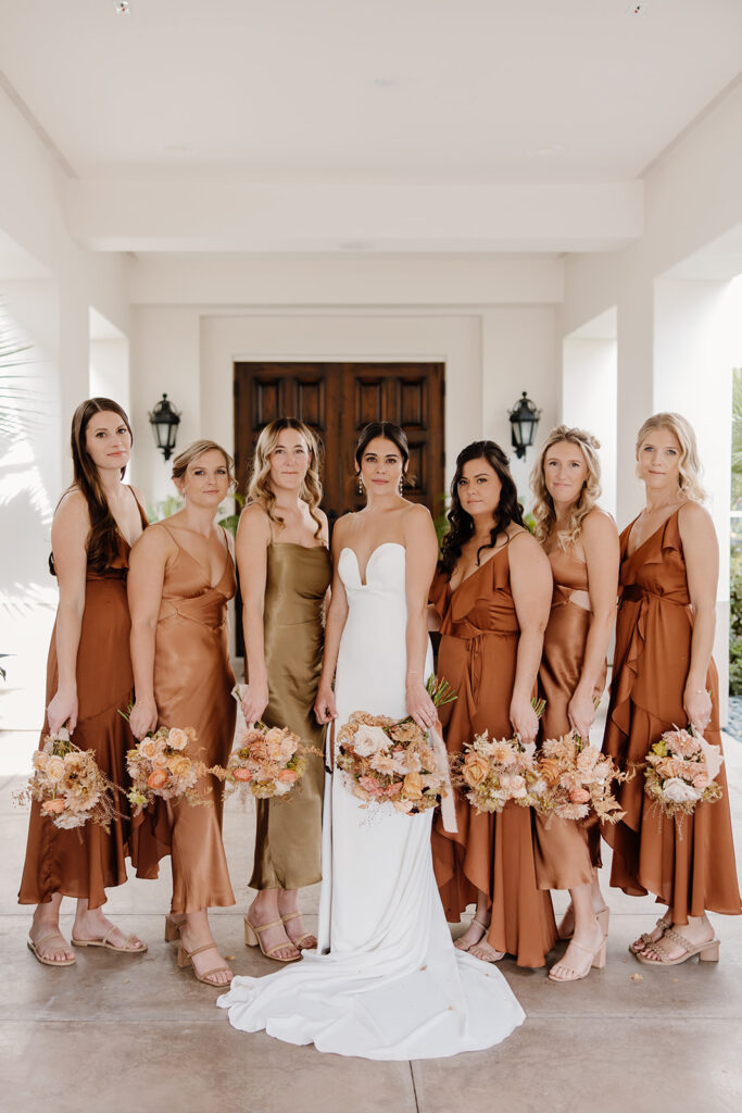 Bride and her bridesmaids holding bouquets wearing rust color dresses