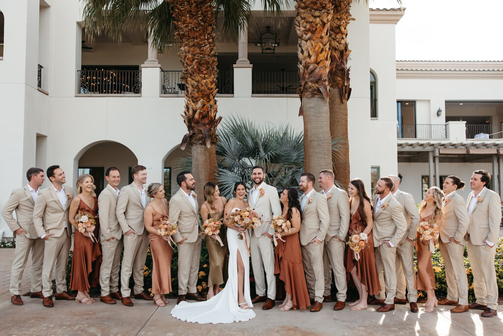 Wedding party with bridesmaids wearing rust and blush dresses and groomsmen wearing tan suits