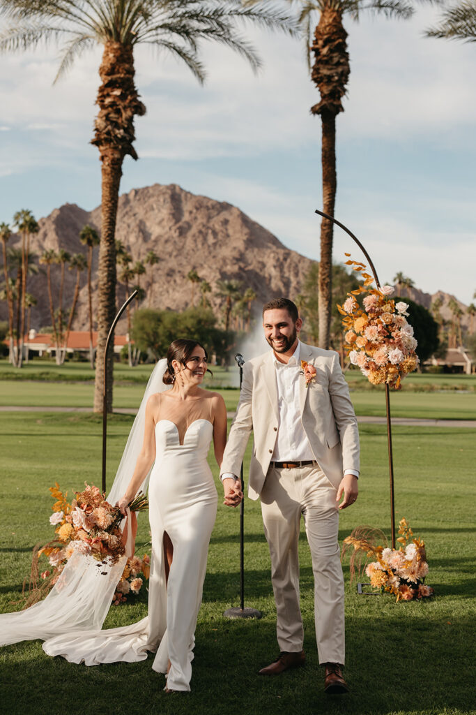 Bride and groom walking in front of their ceremony arch at La Quinta resort