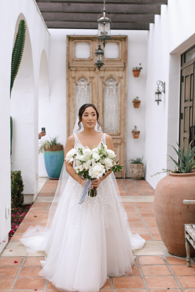 Bride holding a large bouquet with white peonies and greenery at La Ventura Event Center in San Clemente California