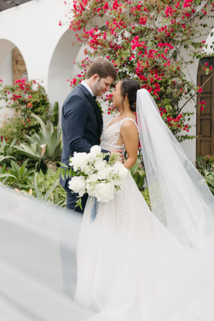 Bride and groom touching foreheads while holding a large bouquet with white peonies and greenery at La Ventura Event Center in San Clemente California