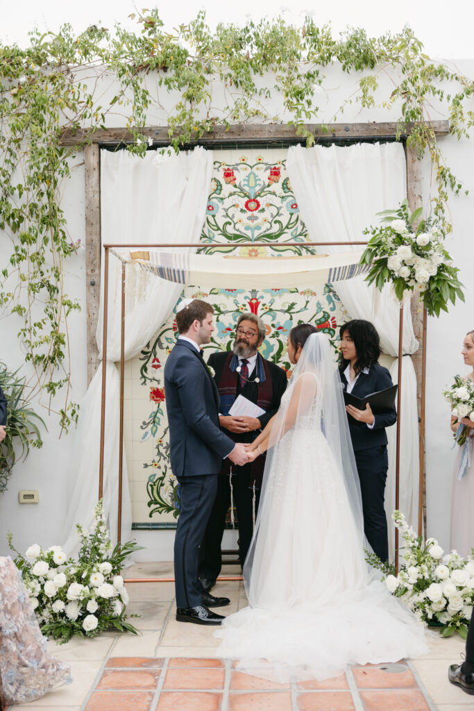 Jewish wedding ceremony at La Ventura Event center with couple standing under their copper Chuppah accented with white flowers and greenery
