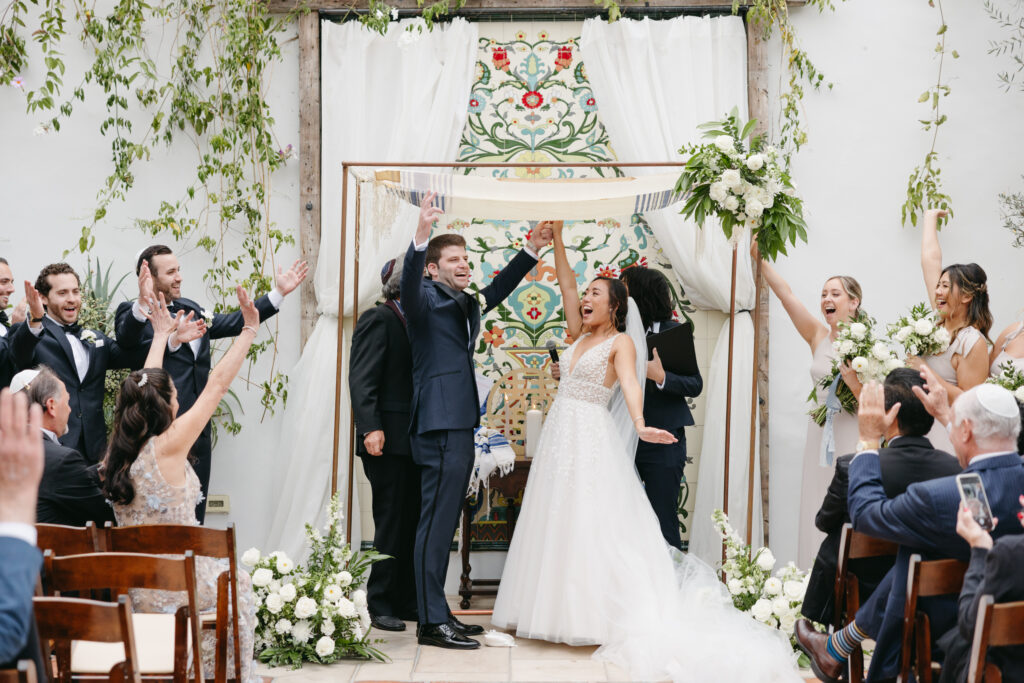 Bride and groom celebrating under their copper Chuppah with white flowers and greenery at La Ventura Event Center