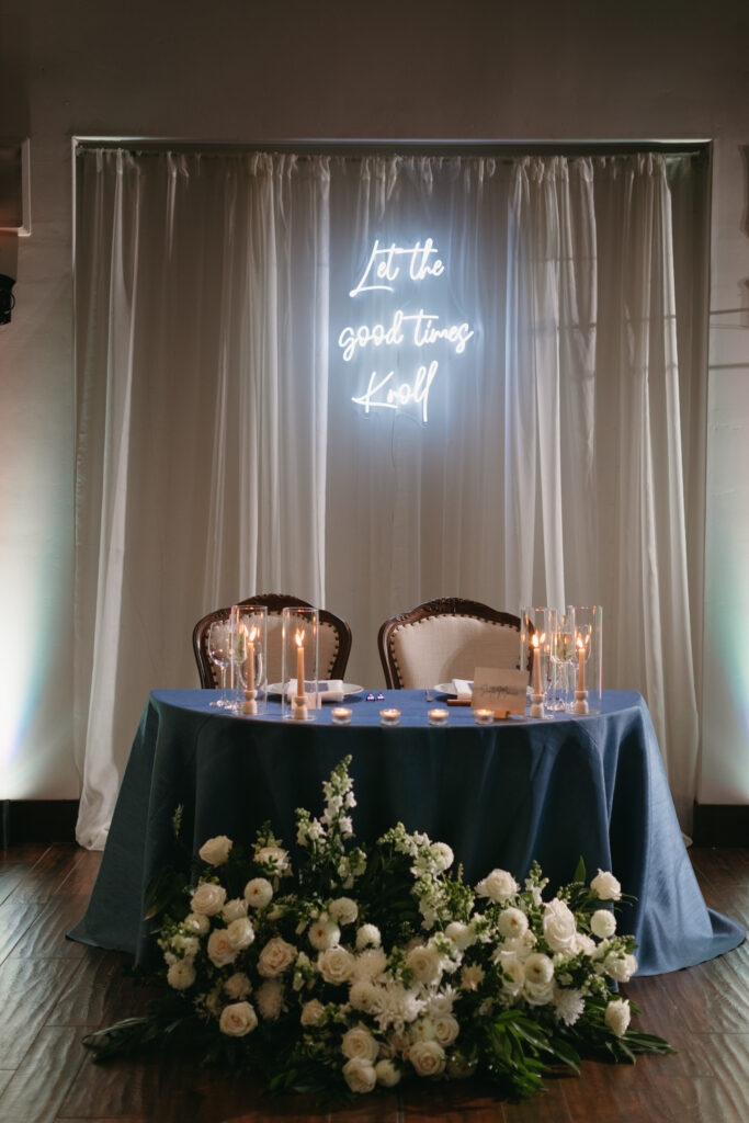 Neon sign hanging over Sweetheart Table with white flowers and greenery accents at La Ventura Event Center in San Clemente California