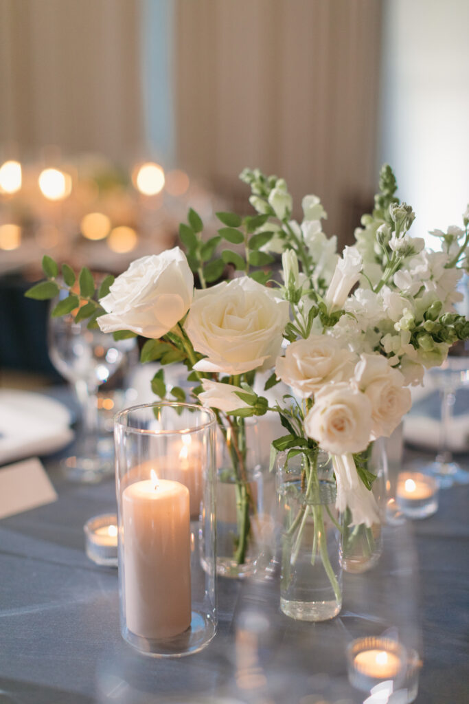Bud vase centerpieces with white flowers and Sandstone pillar candles on blue linen at La Ventura Event Center in San Clemente California