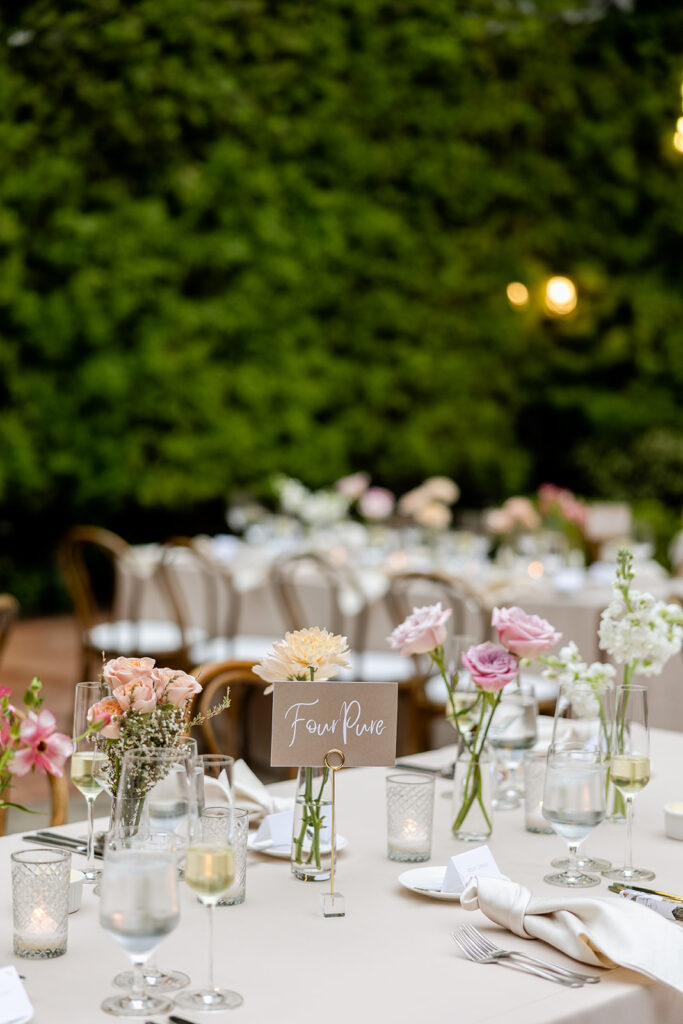 Outdoor wedding reception with long tables with taupe linen and bud vase centerpieces with etched glass votives