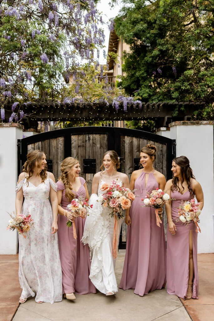Bride and bridesmaids walking in mauve dresses holding bouquets at Franciscan Gardens 
