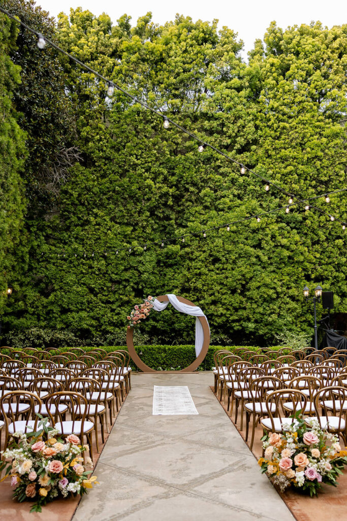 Franciscan Gardens outdoor ceremony with a circle arch draped with white fabric accented by mauve and peach blooms with aisle flowers