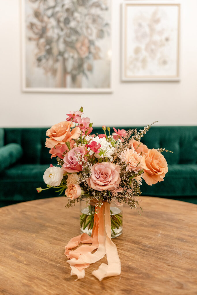 Mauve and peach wedding bouquet with peach silk ribbon on a coffee table in front of a green couch
