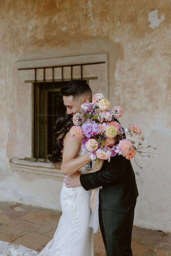 Groom and bride hugging with large colorful summer wedding bouquet
