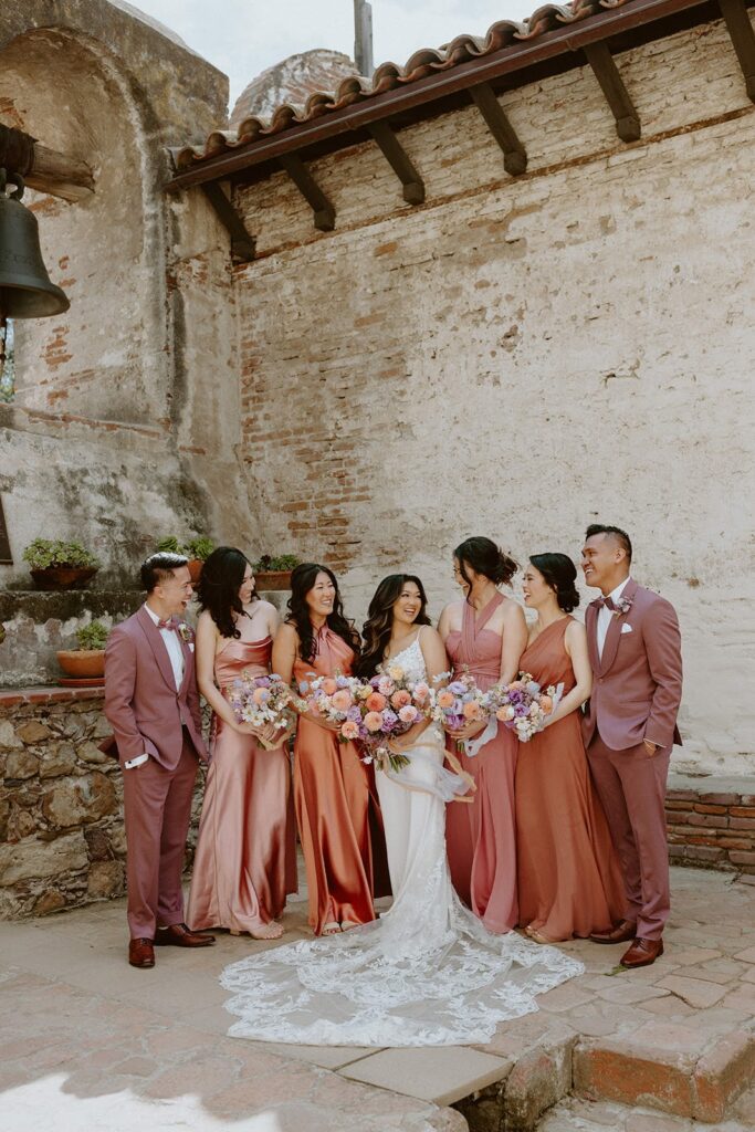 Wedding party wearing mauve and coral dresses and suits with the bride in a lace wedding gown