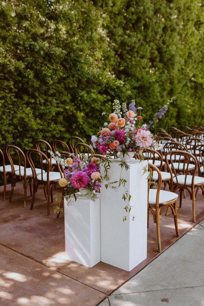 Two colorful floral arrangements on white pillars at different heights