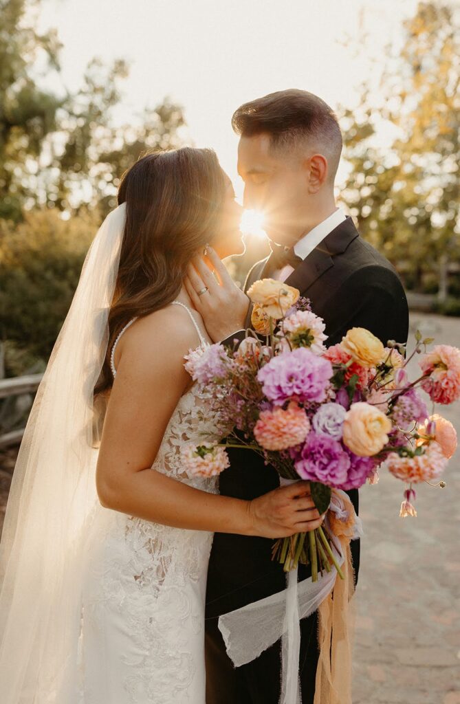 Wedding couple holding a colorful bouquet kissing at sunset