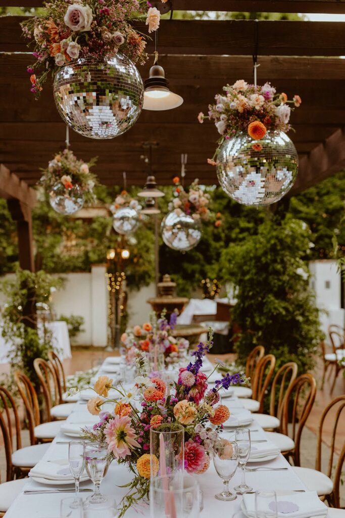 Hanging disco balls with colorful florals over a wedding reception table with bright floral arrangements