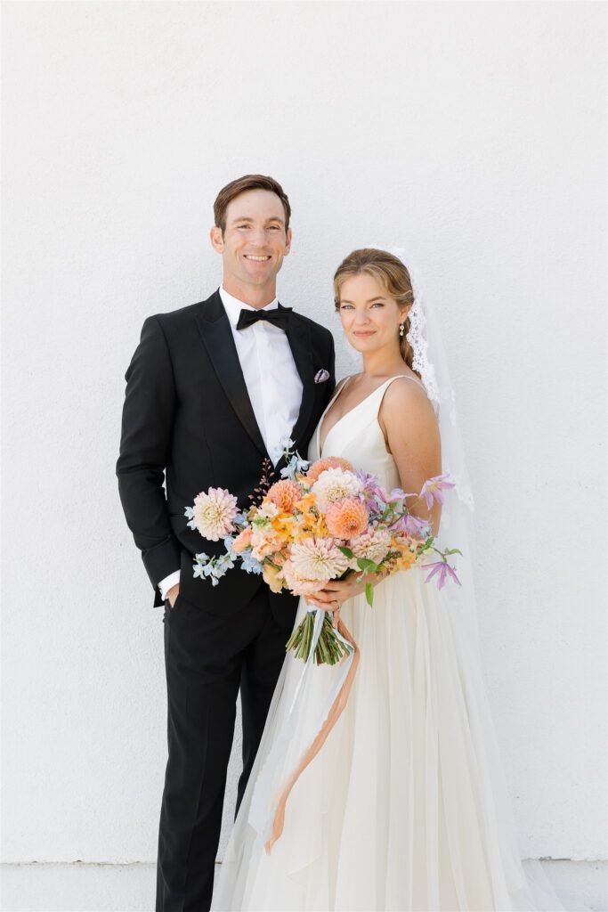 bride and groom against white wall bride holding dahlia bouquet