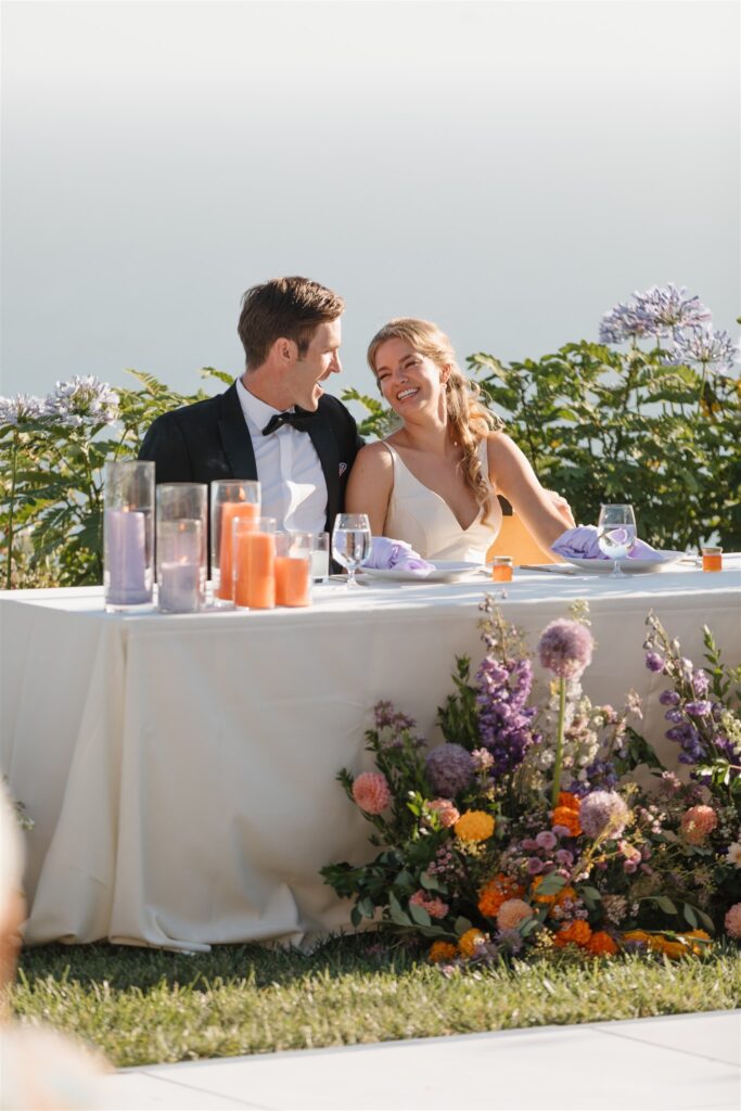 bride and groom at sweetheart table with vibrant flower installation